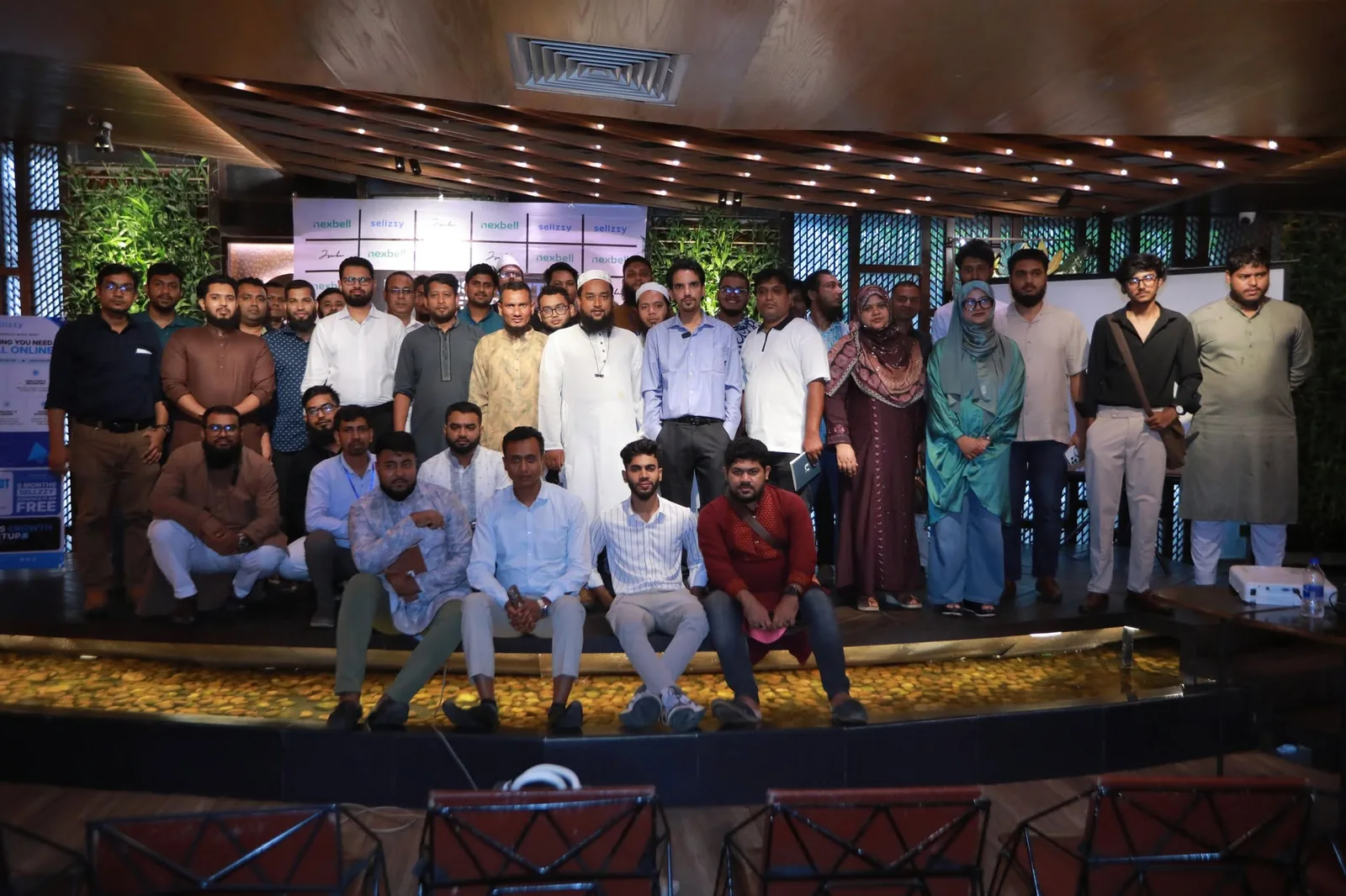 Business Growth Meetup 2026 — অংশগ্রহণকারীদের সাথে দলগত ছবি, পেছনে Sellzzy ও Nexbell পার্টনার ব্যাকড্রপ